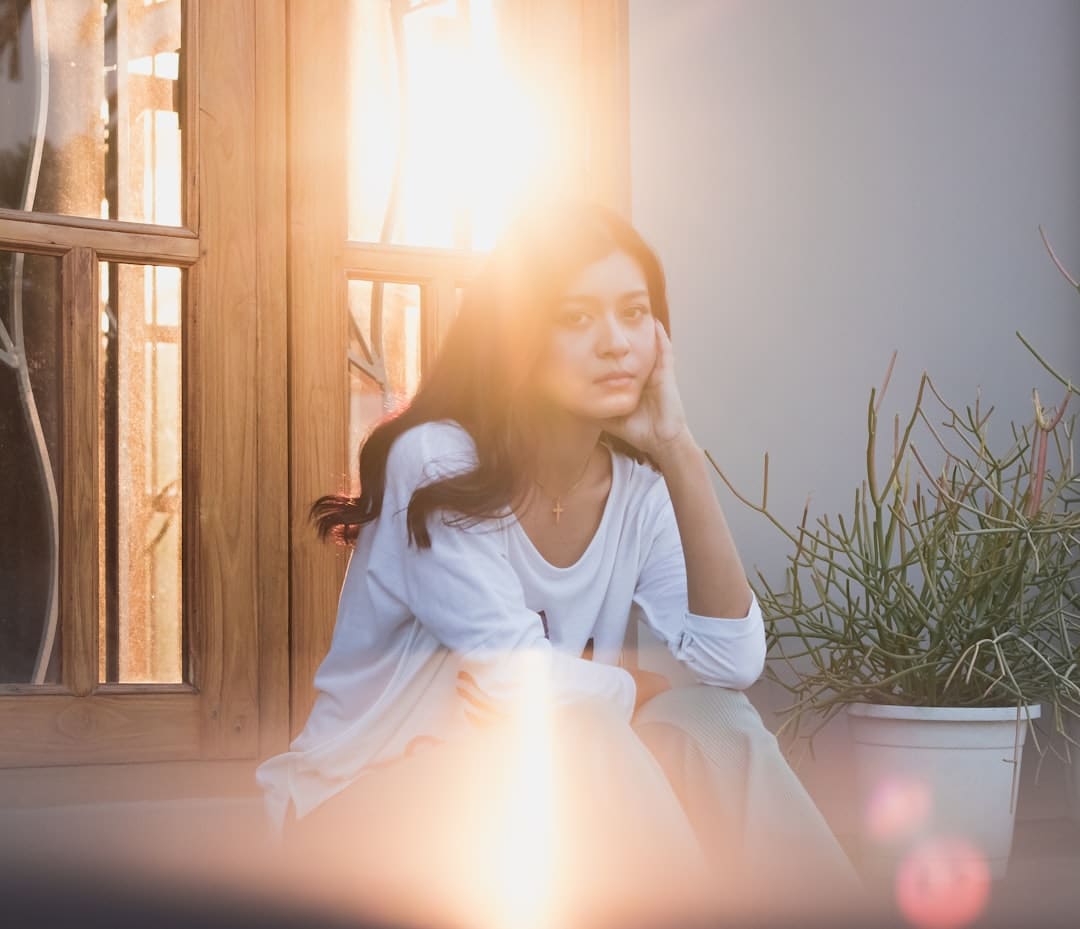 Mujer latina pensativa junto a una ventana, iluminada por la luz del sol